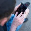 A man in casual attire checks cryptocurrency prices on his smartphone outdoors.